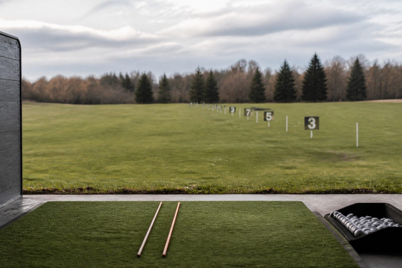 Driving range bay with two alignment sticks laid on the turf and a row of numbered target flags at different distances down the range